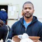 Man holding box of donated groceries outdoors at food bank